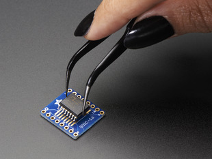 A pair of tweezers holding a microchip hovers over the SMT Breakout PCB for SOIC-16 or TSSOP-16.