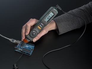 White hand holding a Autoranging Digital Multimeter Pen against an Arduino. Pen reads 4.91.