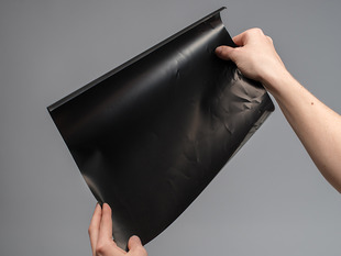 Angled shot of white hands holding up a black Pressure-Sensitive Conductive Sheet.