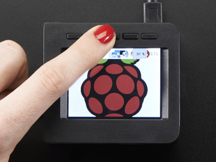 Top-down shot of assembled 2.4" PiTFT HAT. A red manicured finger presses a button above the display which shows a raspberry logo.