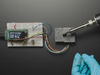 Person soldering next to sensor, which detects the fumes and shows air quality on OLED
