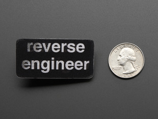 straight down view of black rectangular badge with the words REVERSE ENGINEER in white, next to a quarter for scale. 