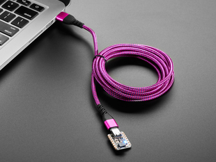 Angled shot of a pink/purple woven USB cable plugged into a laptop port and a small dev board.