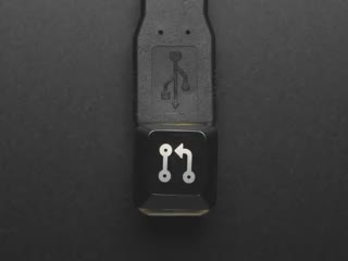 Top view video of black Pull Req keycap connected via USB cable. Various colors emit through the logo.