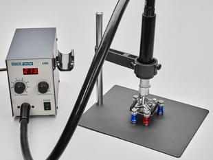 Angled shot of a hot air station air gun attached to a metal pole and clamp above a PCB.