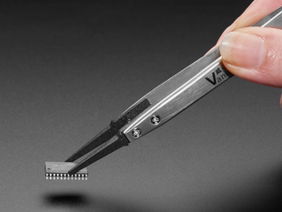 Lifestyle image of gray tweezers picking up a microchip.