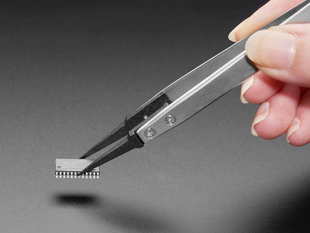 Lifestyle image of a white hand picking up a microchip with tweezers.