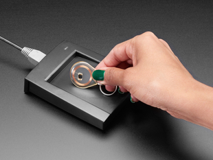 Hand touching clear RFID tag to enclosed reader